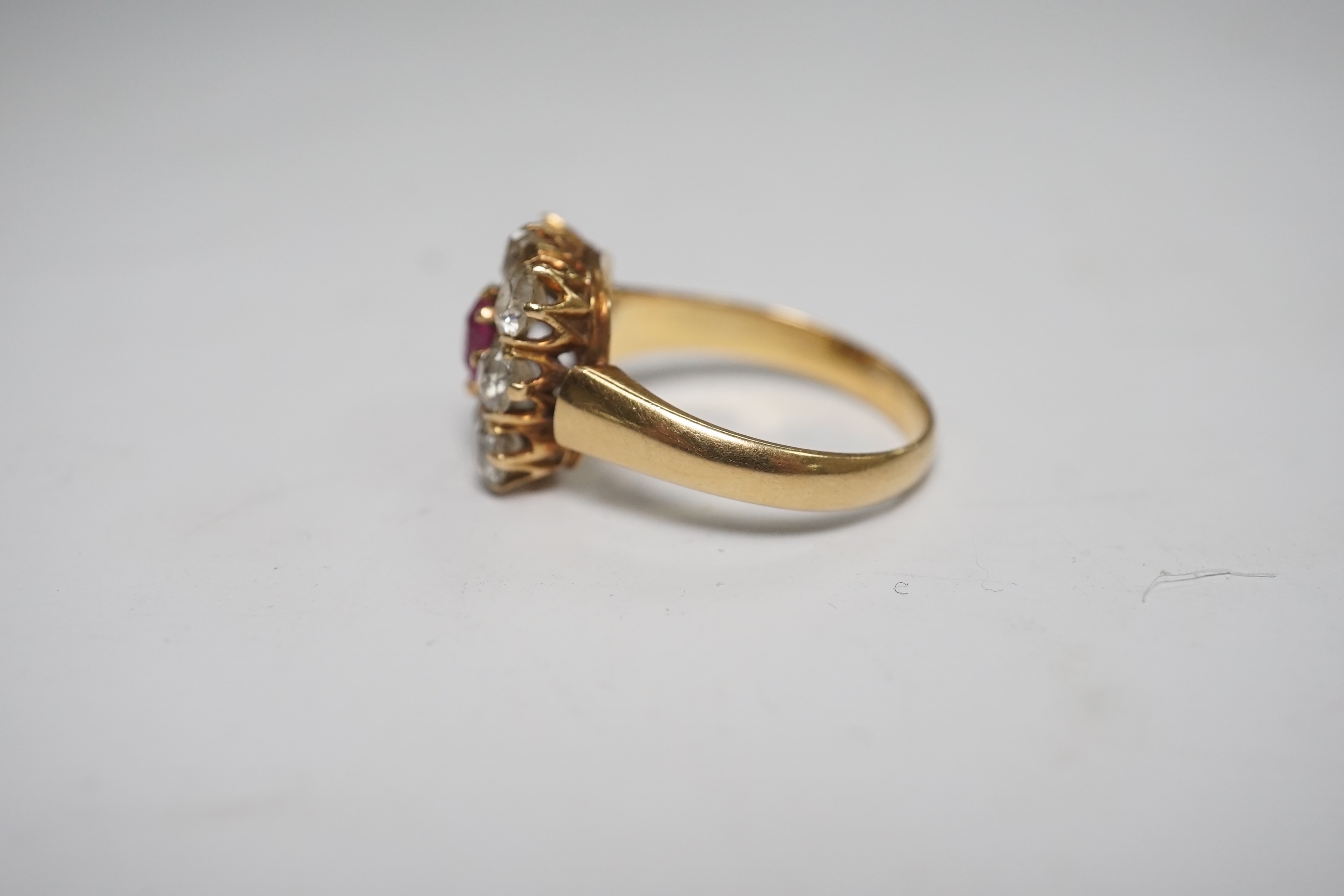 An early 20th century yellow metal, single stone ruby and eight stone diamond set square cluster ring, size O, gross weight 5 grams, one diamond missing. Condition - poor to fair